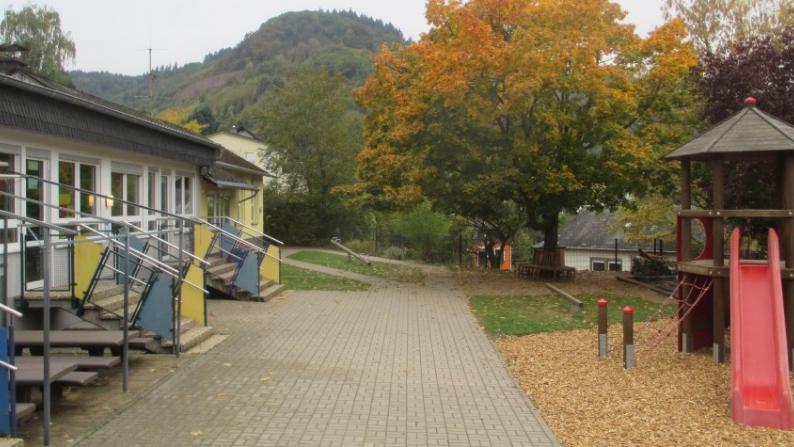 Außenfoto der Einrichtung mit Spielturm und Eingangsbereich. Bäume im Hintergrund