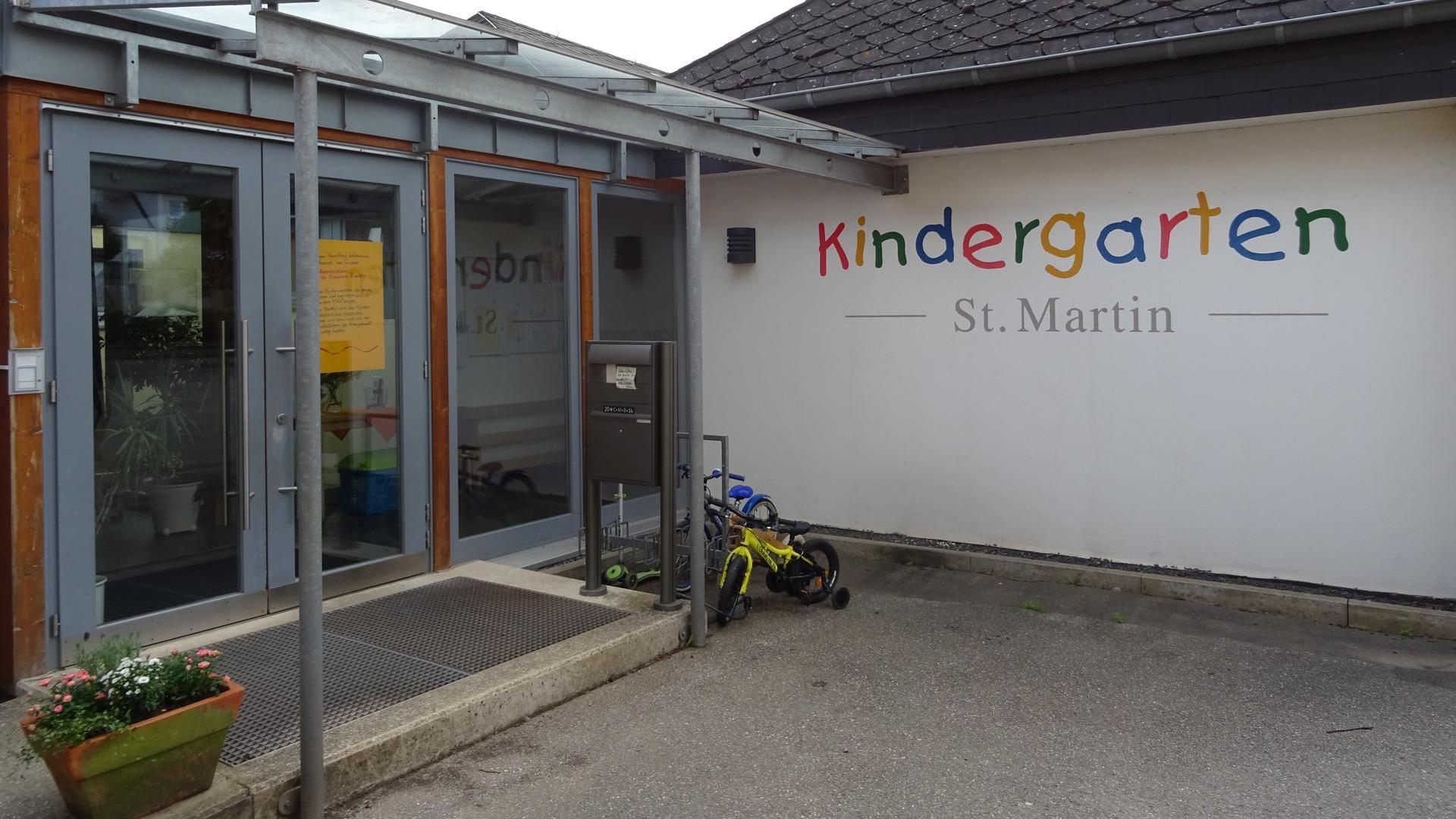 Man sieht den Eingangsbereich der KiTa. An der Wand steht in bunten Lettern das Wort Kindergarten.