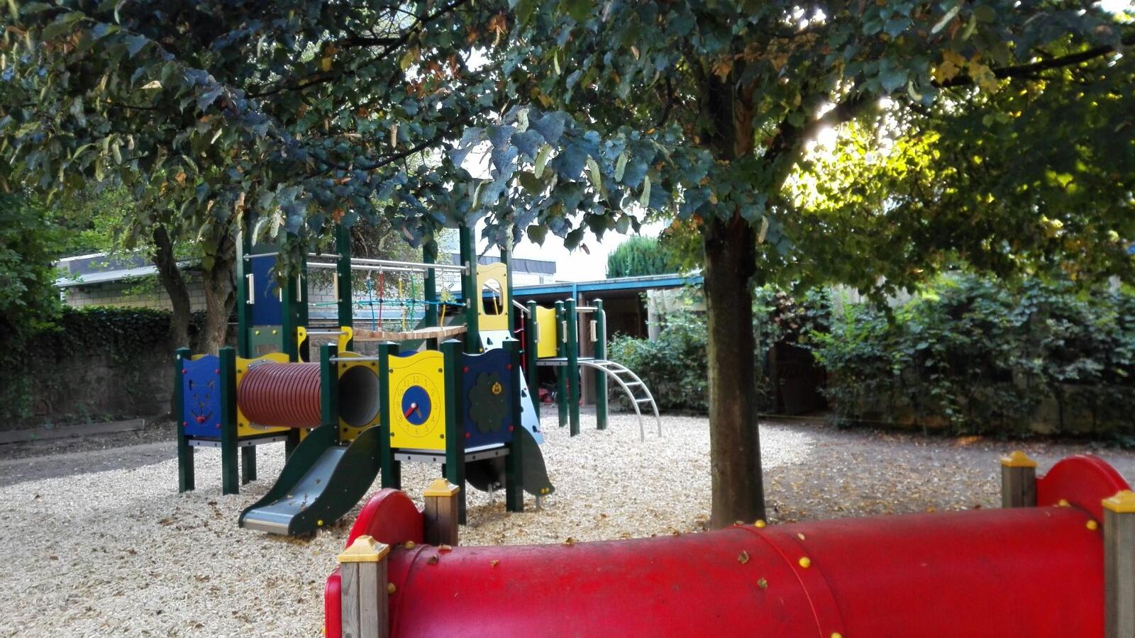 Man sieht den Spielplatz mit einem roten Tunnel vorne und ienem Klettergerüst in der Mitte