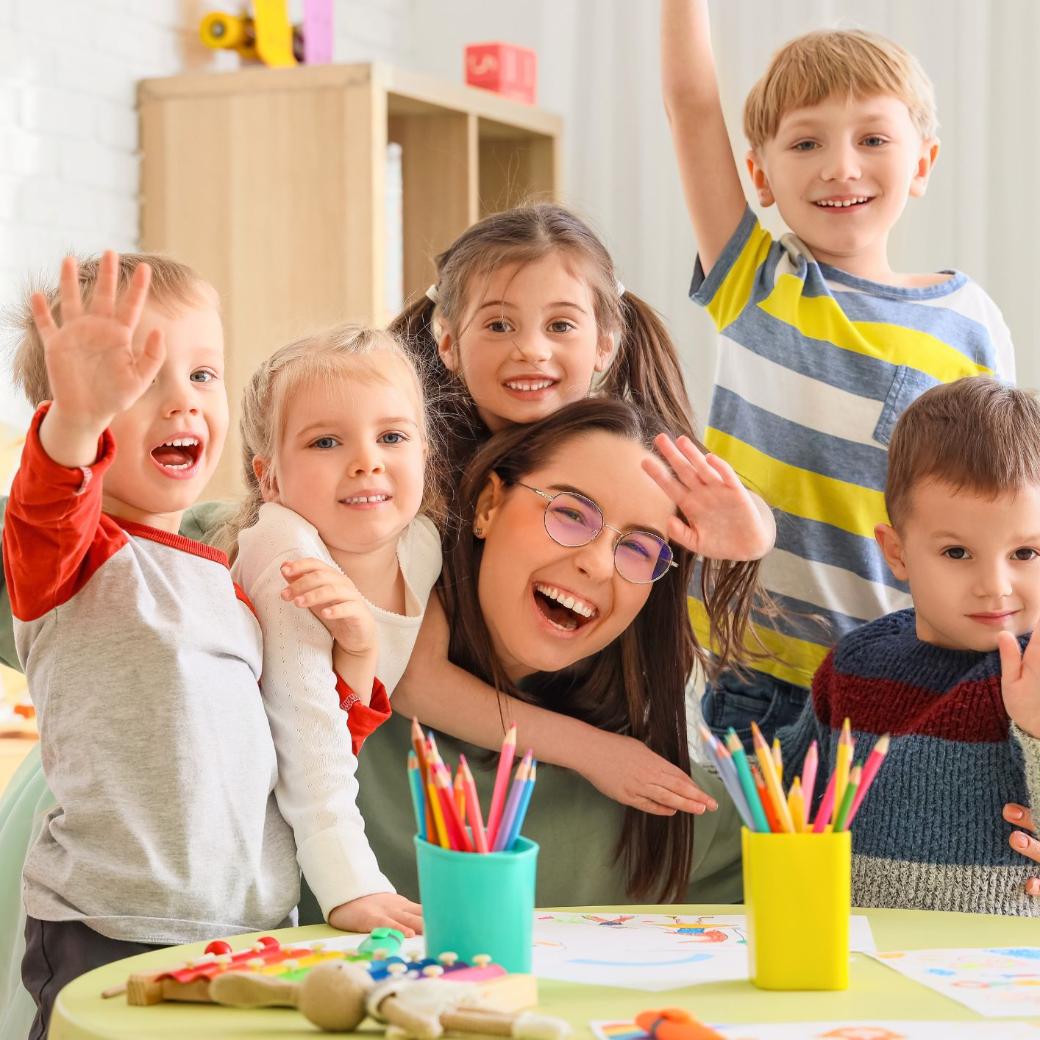 Man sieht lachende und winkende Kinder rund um eine glückliche Erzieherin