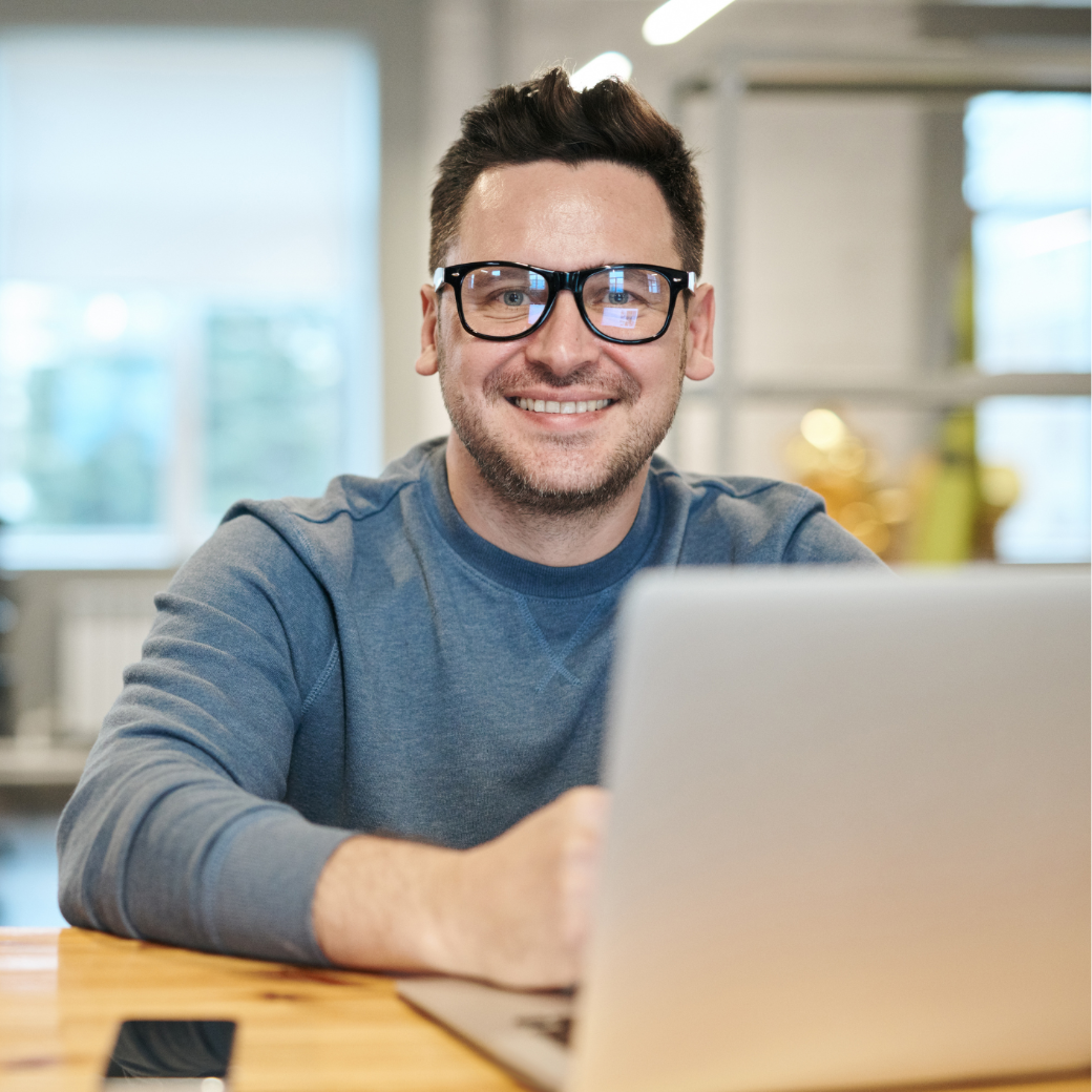 Lächelnder Mann mit Brille sitzt am Laptop