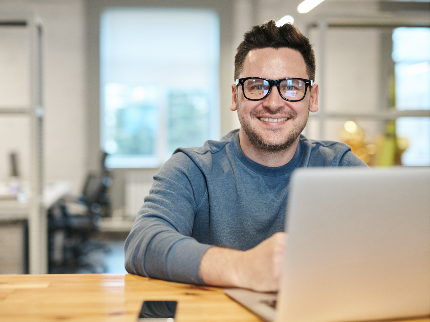 Lächelnder Mann mit Brille sitzt am Laptop