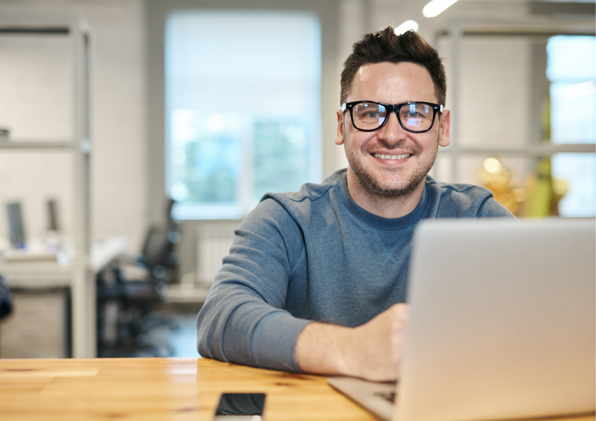 Lächelnder Mann mit Brille sitzt am Laptop